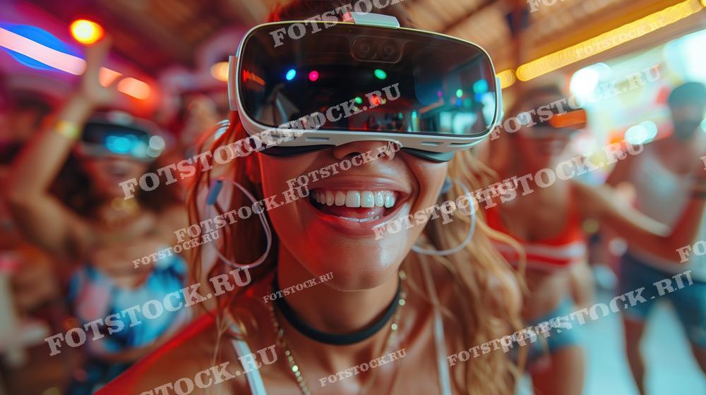На фотографии изображена женщина в виртуальных очках, улыбающаяся и наслаждающаяся вечеринкой. Вокруг нее люди, погруженные в виртуальную реальность, создают атмосферу веселья.