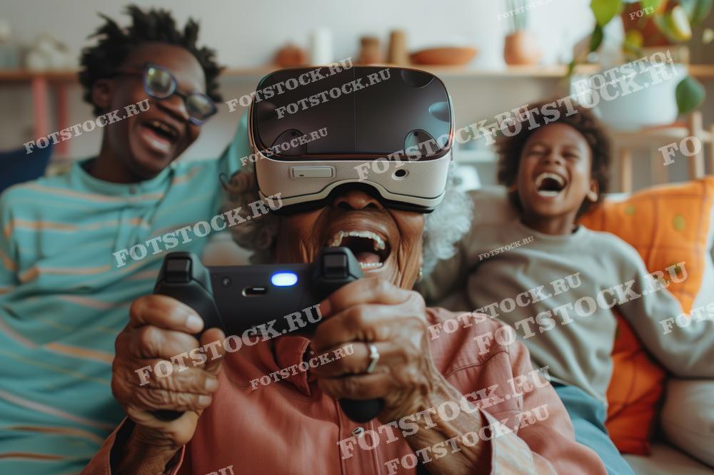 На фотографии изображена пожилая женщина в виртуальных очках, играющая с геймпадом. Рядом с ней смеются двое детей, создавая атмосферу радости и семейных развлечений с использованием современных технологий.