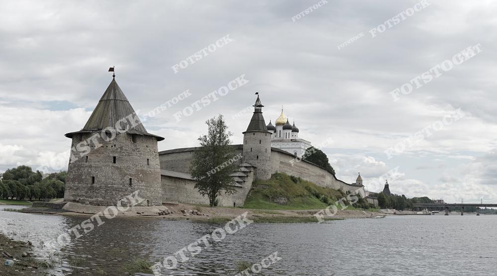 На фотографии изображён Псковский кремль с его башнями и золотыми куполами собора. Река подчёркивает гармонию архитектуры и природы, а облачное небо добавляет драматичности пейзажу. Это символ исторической и культурной значимости Пскова.