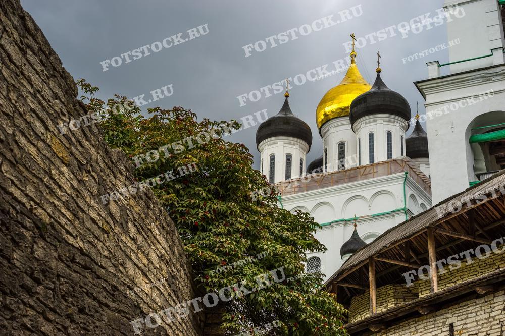 На фотографии изображены купола Троицкого собора, расположенного в Псковском Кремле. Золотые и черные купола контрастируют с каменными стенами, подчеркивая величие православной архитектуры и культурного наследия России.