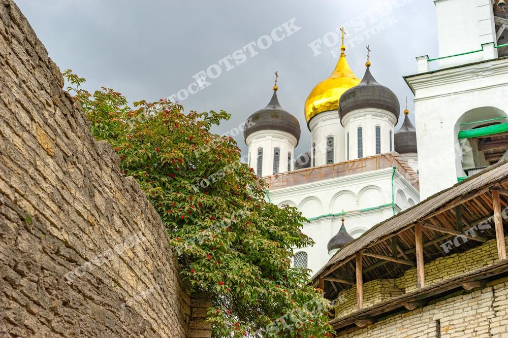 На изображении Троицкий собор в Пскове, его золотые купола видны за старинной стеной монастыря. Это символ культурного и религиозного наследия города, сочетающий в себе элементы исторической архитектуры и природного окружения.