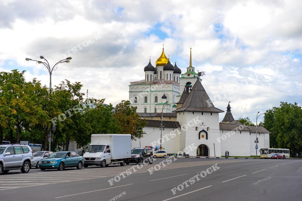 На фото изображен Псковский кремль с Троицким собором, расположенный рядом с городской улицей. Современные автомобили и уличные фонари сочетаются с историческими архитектурными элементами, создавая интересное сочетание прошлого и настоящего.