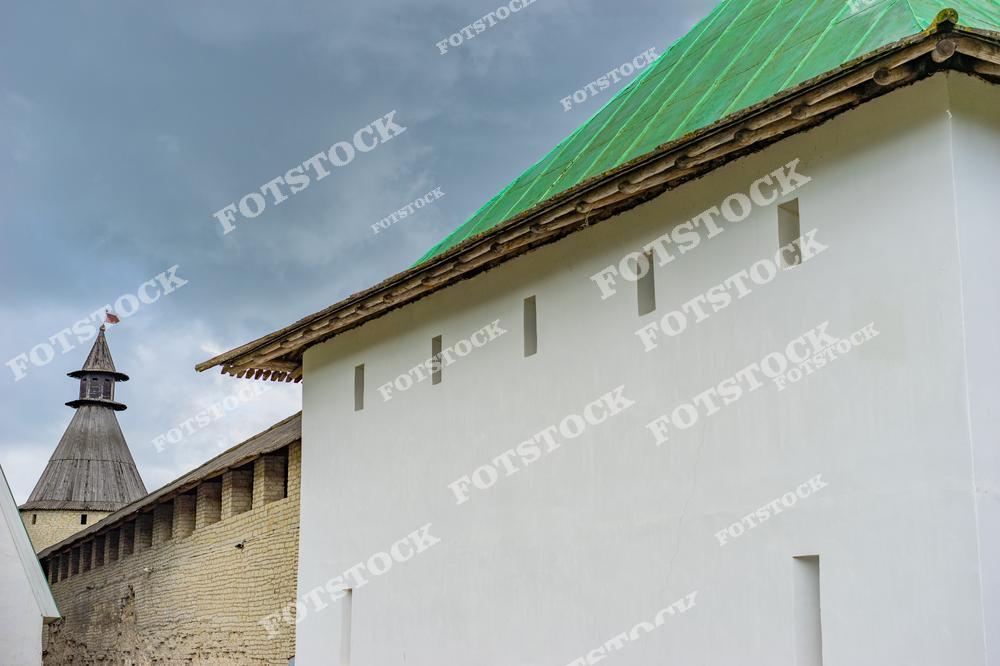 На фотографии изображена часть Псковского кремля, где видна белая стена и деревянная башня с флагом. Реставрационные работы подчеркнули историческую значимость этой крепости.
