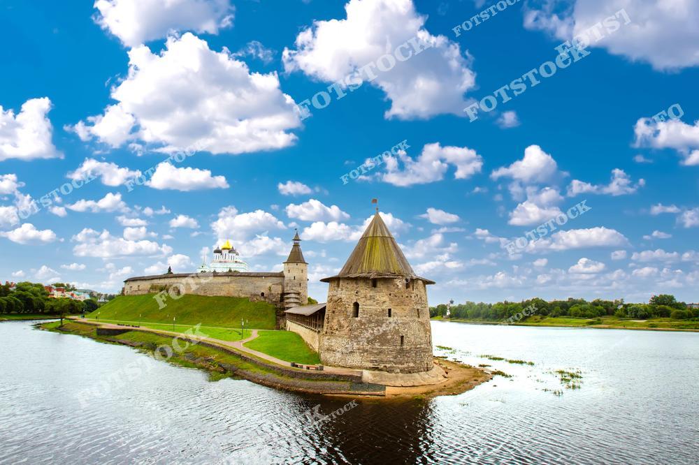 На фотографии изображён Псковский Кремль, расположенный на берегу реки Великой. Центральное место занимает башня, а на заднем плане виден собор с золотыми куполами. Голубое небо с белыми облаками и отражения в воде создают атмосферу гармонии и спокойствия.