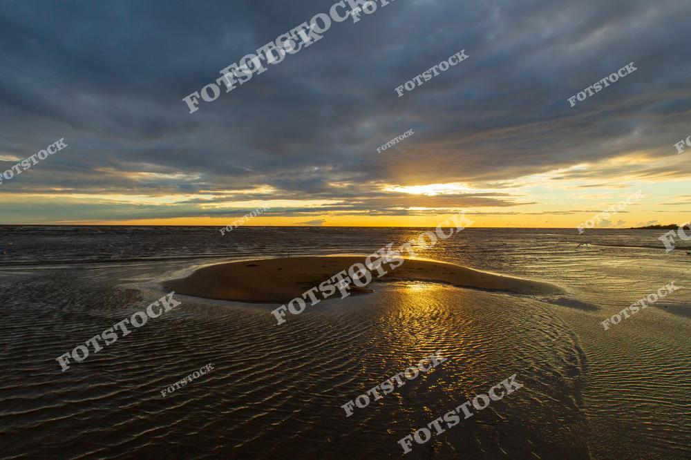 На фотографии запечатлен закат на Чудском озере, где свет солнца отражается на воде. На переднем плане видна песчаная отмель, а небо украшено драматическими облаками. Этот пейзаж символизирует красоту и спокойствие природной гармонии.