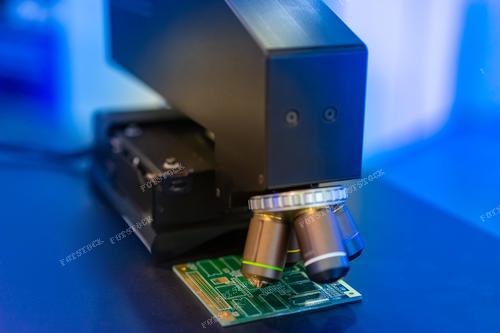 На фотографии представлены процессы работы с печатными платами (PCB) и тестирования микросхем. Оборудование для проверки и создания микросхем, а также микроскоп, сфокусированный на электронной плате, занимают центральное место. Этот снимок иллюстрирует промышленные процессы производства компьютерных чипов и внедрения новых технологий в области компьютерной инженерии.