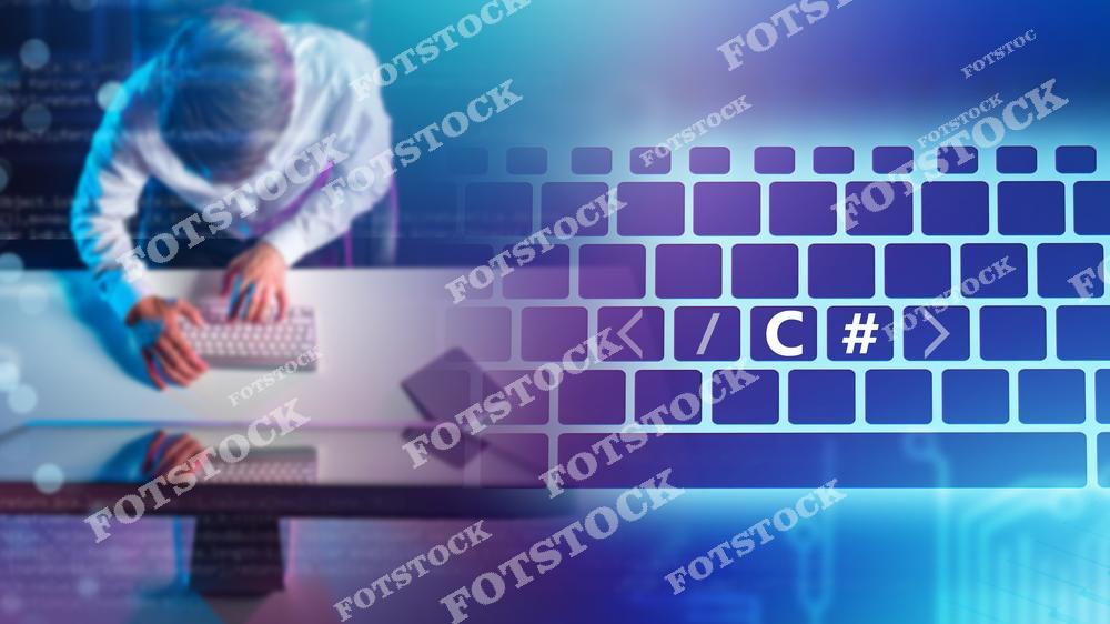 На снимке изображен программист, работающий за компьютером, в окружении абстрактных цифровых элементов и клавиатуры с выделенным текстом «C#». Фотография иллюстрирует процесс написания программного кода и создание решений на языке программирования C#.
