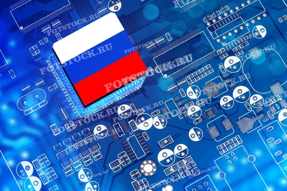 На фотографии изображен микрочип с изображением флага России на фоне электронной платы. Фотография символизирует технологическое развитие и инновации в сфере электроники в России.