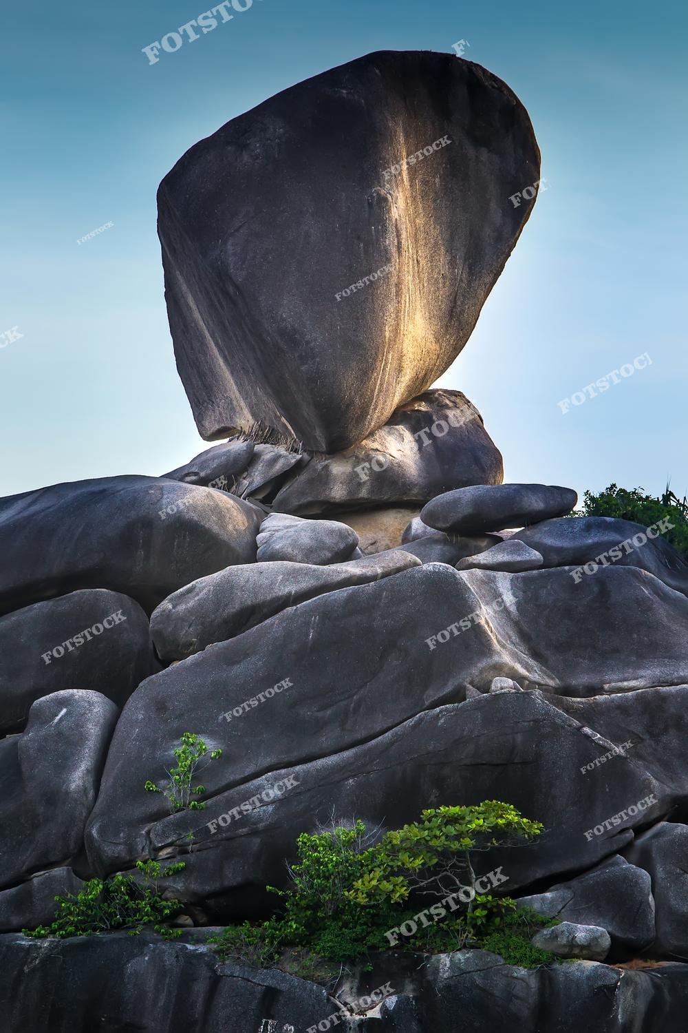 Фотография демонстрирует скалу Парус (Sail Rock) на одном из Симиланских островов в Таиланде — знаковый природный объект, возвышающийся над тропическим побережьем. Массивный камень будто балансирует на вершине гранитных валунов и подсвечен мягким закатным светом. Это место считается визитной карточкой Симилан и популярно среди туристов и фотографов.