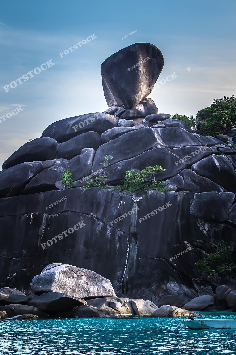 Фотография демонстрирует скалу Парус (Sail Rock) на Симиланских островах в Таиланде, снятую с моря. На переднем плане — прозрачная бирюзовая вода, обрамляющая массивные гранитные валуны. Эта природная композиция стала визитной карточкой Симиланского архипелага и одним из самых популярных мест для посещения в национальном парке.