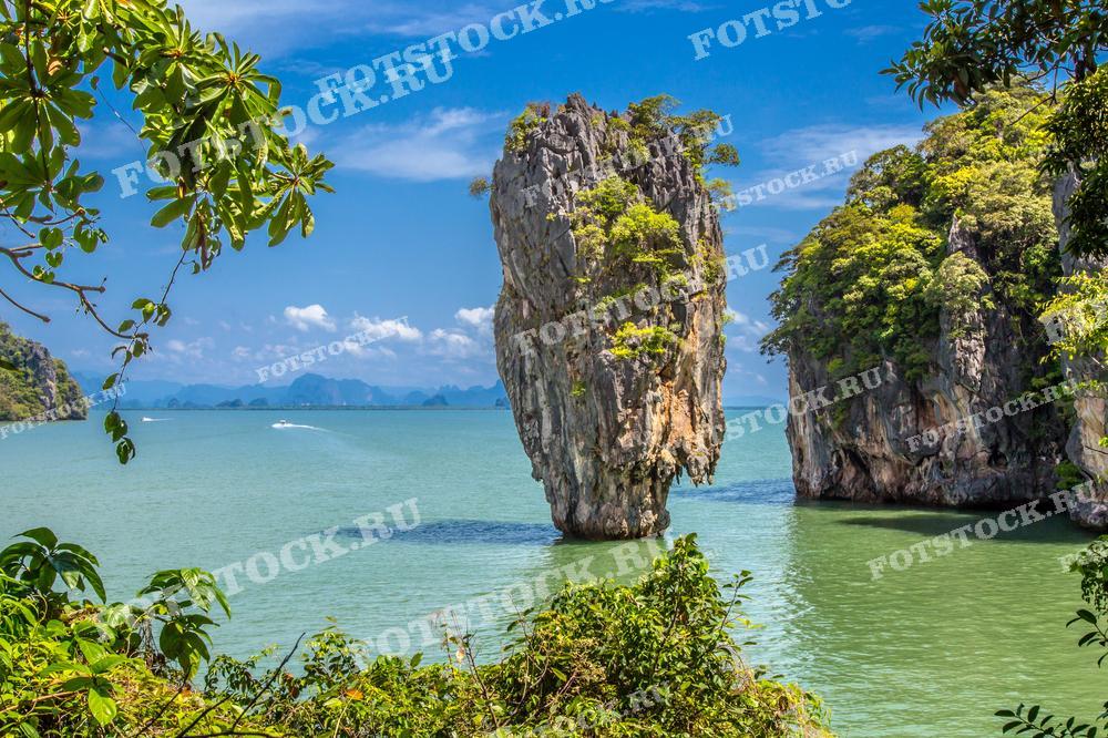 На изображении остров Джеймса Бонда в заливе Phang Nga, Таиланд. Скала возвышается из воды, окружённая тропической растительностью и бирюзовыми волнами. Вид на остров подчёркивает природную красоту и экзотичность местности, создавая ощущение спокойствия и умиротворения.