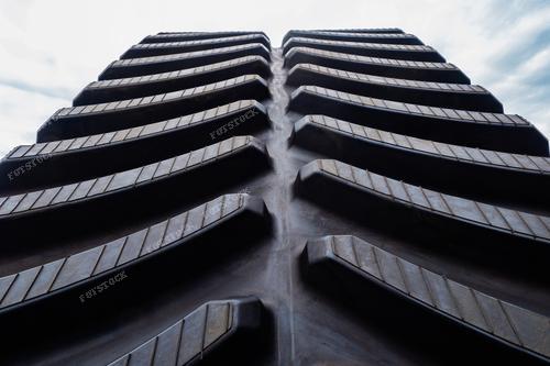 Крупным планом изображен протектор колеса трактора. Фотография символизирует запасные части для тракторов. Колесо стоит на фоне неба. Высокий протектор колеса гарантирует высокую проходимость трактора на поле и других грунтах.