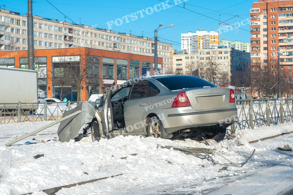 На фотографии изображен автомобиль с поврежденной задней частью и открытой дверью, стоящий на заснеженной улице в городе. Видны окружающие здания и дороги. Сцена иллюстрирует последствия аварии в зимних условиях.