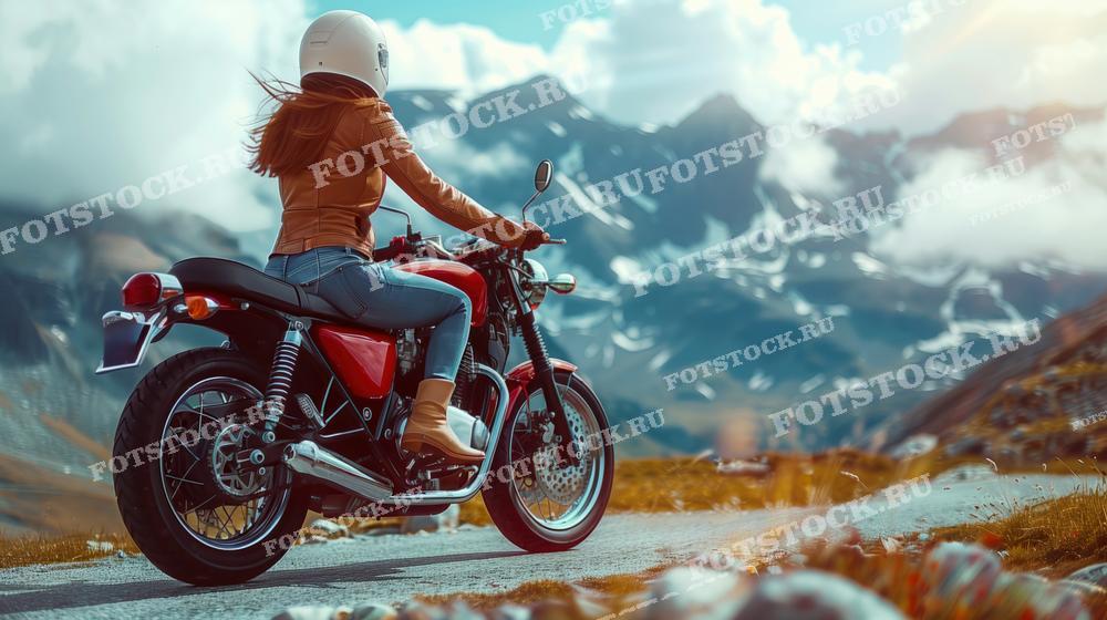На фотографии изображена женщина в шлеме, сидящая на мотоцикле на горной дороге. Она смотрит вдаль на заснеженные вершины и облака, окружающие горы. Сцена передает ощущение свободы, приключения и наслаждения природой во время путешествия на мотоцикле.