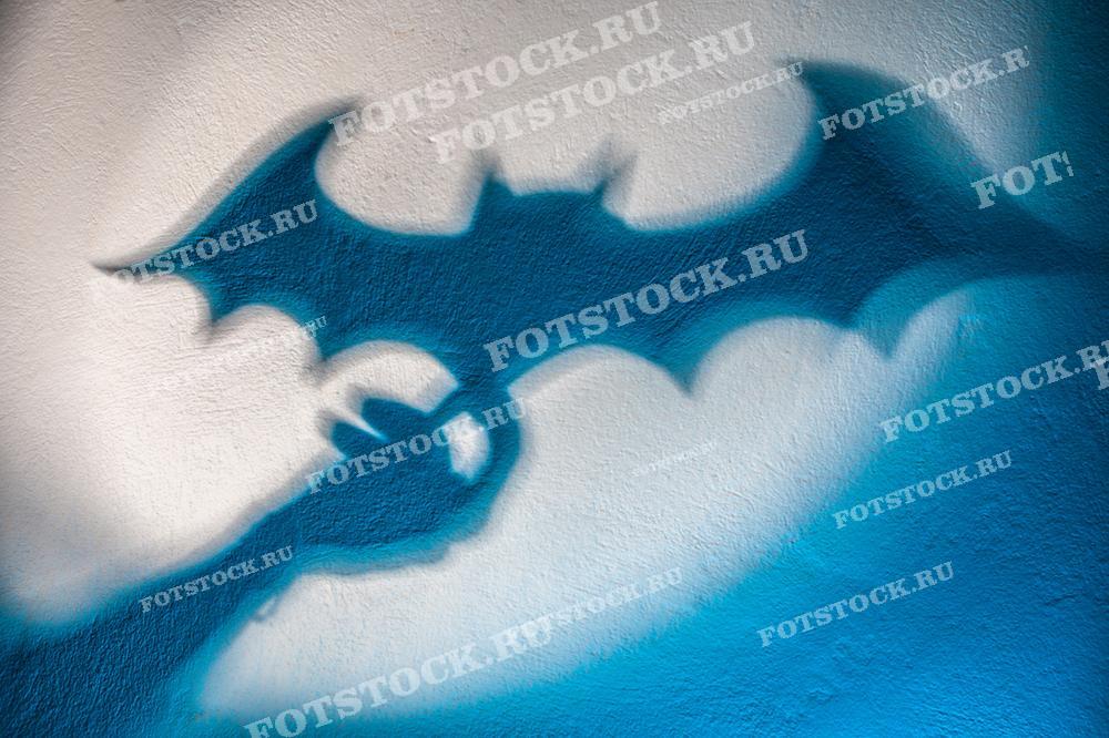 Фотография показывает граффити, изображающее летучую мышь на стене. Темные силуэты на светлом фоне создают контраст, типичный для уличного искусства.