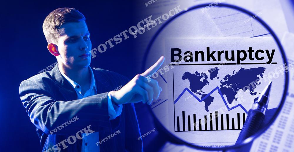 На фотографии изображен молодой мужчина, указывающий на график с текстом "Bankruptcy". Изображение символизирует анализ финансовых проблем и банкротства на глобальном уровне.