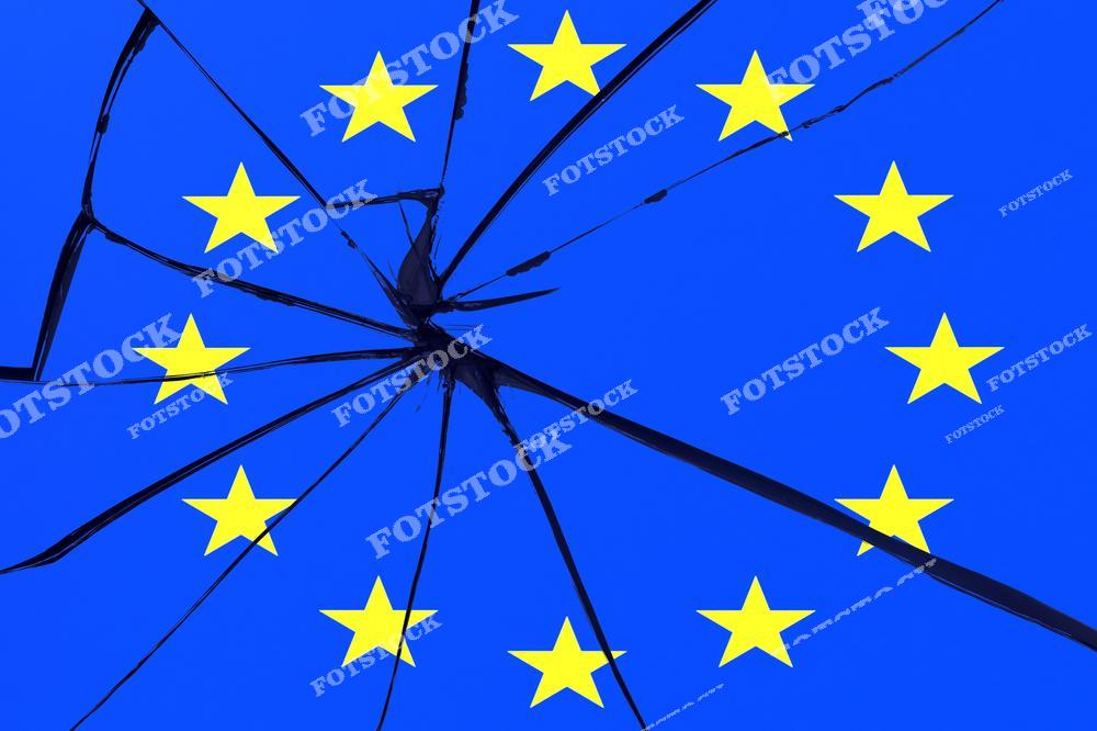 На изображении флаг Европейского Союза с характерными желтыми звездами на синем фоне, покрытый эффектом треснувшего стекла. Это визуализирует тему раскола, кризиса и проблем внутри Евросоюза.