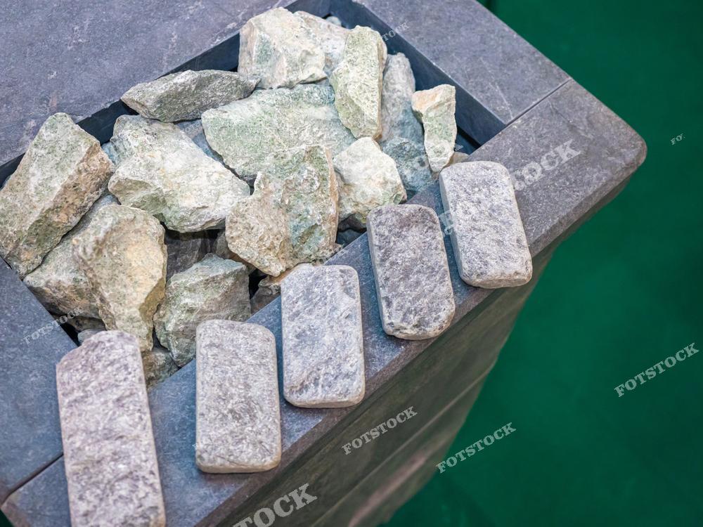 На фотографии изображены камни для банной печи, расположенные на плиточной конструкции. Камни разных размеров и оттенков создают текстурный контраст с гладкой поверхностью. Снимок подчёркивает элементы банной культуры и традиций.