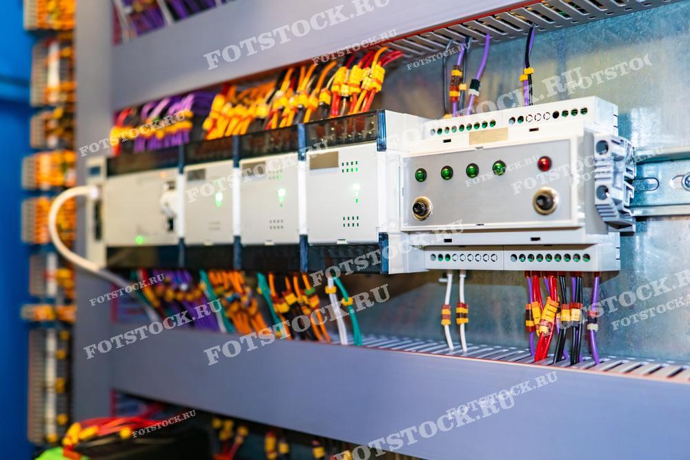 Внутренний вид распределительного шкафа с множеством проводов и контроллеров, подключенных к различным модулям. Система используется для управления и мониторинга электрических цепей в промышленности или на крупных объектах.