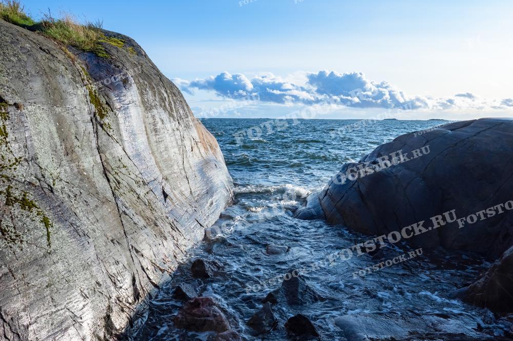 На фотографии запечатлен красивый пейзаж природы Финляндии. Волны бьются о камни, создавая динамичную и живописную сцену. Такие изображения отлично подходят для иллюстрации статей о природе, в блогах о путешествиях, экологических исследованиях, а также могут быть использованы в рекламных и образовательных материалах.