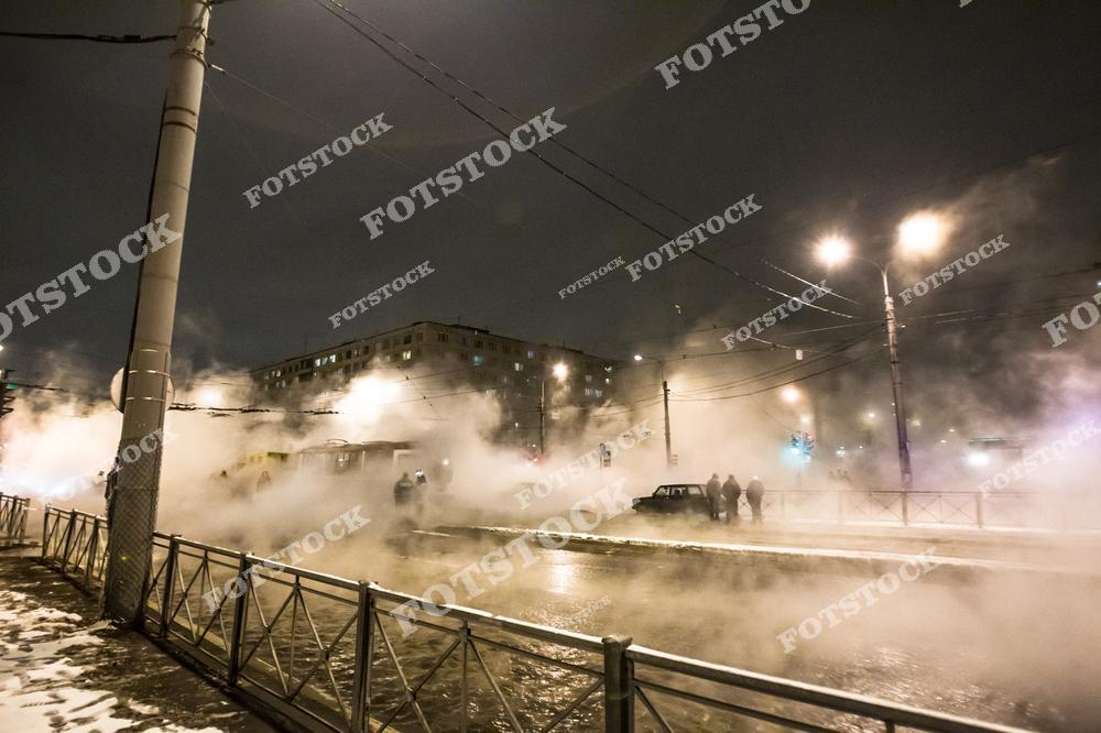 На фотографии показан городской участок улицы с сильным выбросом пара из-за прорыва горячей воды. Образовавшийся туман создает плотную дымку, через которую едва видны люди и машины. Это изображение иллюстрирует аварийную ситуацию на теплосетях.