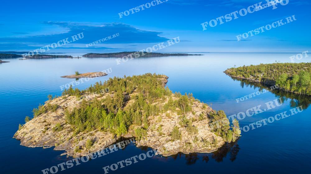 На этой фотографии представлена панорама озёрных шхер Карелии, снятая с высоты. Ярко-голубая гладь воды окружает покрытые лесом скалистые острова, создавая живописный и спокойный пейзаж. Чистота воды и нетронутая природа делают этот снимок прекрасным материалом для экологических публикаций, туристических буклетов и календарей, а также для иллюстрации веб-сайтов, посвященных природе и путешествиям.