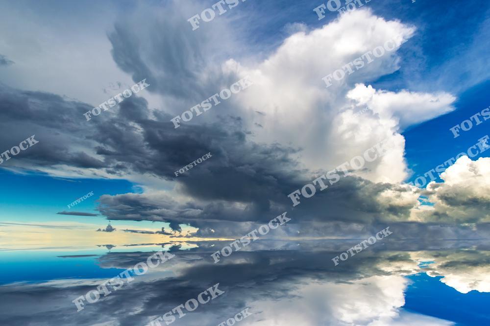 Фотография запечатлела мощные грозовые облака, нависшие над Ладожским озером. Их отражение в спокойной воде создает эффект бесконечного неба. Контраст между темными тучами и яркими участками голубого неба подчеркивает динамику природной стихии. Этот снимок передает величие и переменчивость карельского климата, привлекая внимание к красоте облачных образований.
