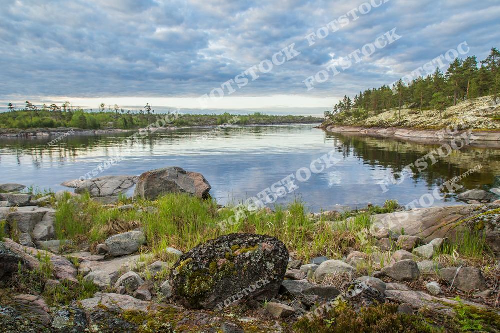 Это изображение побережья Ладожского озера, одного из самых крупных и красивых озёр Европы, расположенного в Карелии. Скальные образования, обрамляющие береговую линию, добавляют величия этому живописному уголку природы. Летний день раскрывает все краски природы Карелии, где сочетаются прозрачные воды Ладоги и зелёные просторы, создавая атмосферу спокойствия и умиротворения. Этот регион известен своими уникальными природными пейзажами и является популярным местом для путешественников, любящих отдых на природе и прогулки по водоёмам.