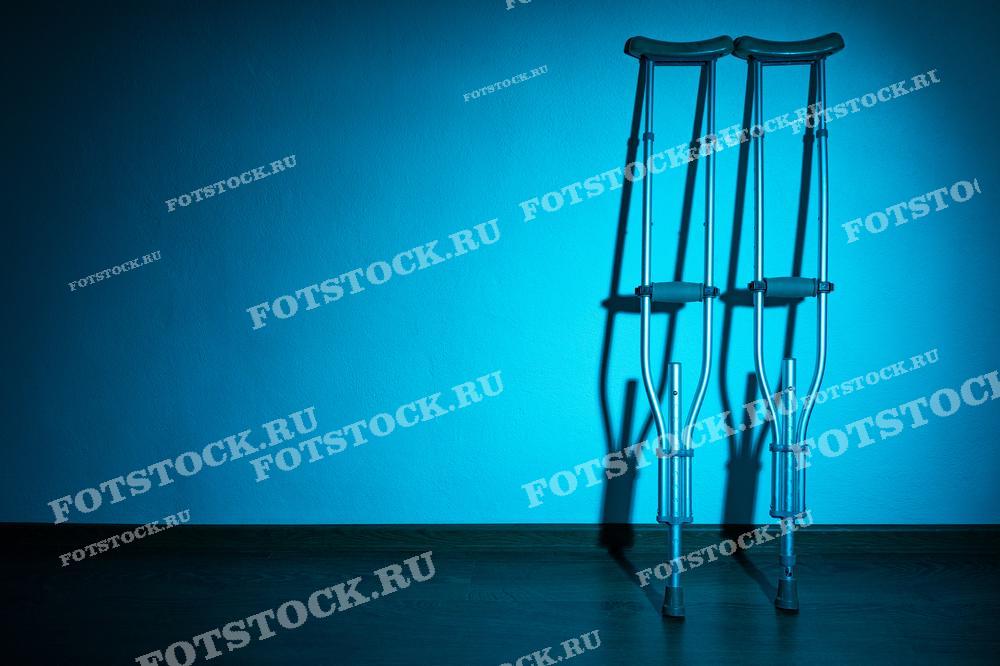 На изображении пара костылей, прислонённых к стене, освещённая мягким синим светом. Сцена передаёт ощущение реабилитации после травмы или болезни.
