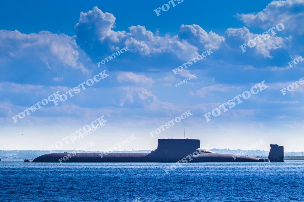 На фотографии изображена подводная лодка, находящаяся на поверхности моря под ярким голубым небом с облаками. Судно символизирует современные технологии военно-морского флота и обороны. Снимок подчёркивает величие и стратегическую важность морских технологий.
