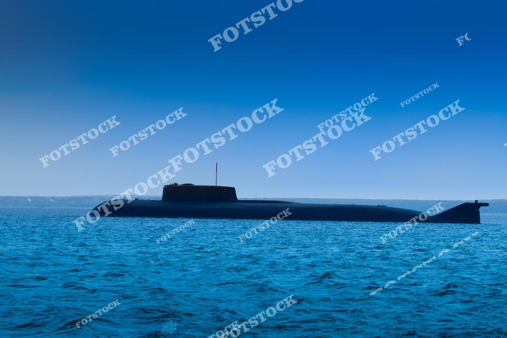 На фотографии изображена подводная лодка, движущаяся по спокойной поверхности моря на фоне горизонта. Её силуэт подчёркнут насыщенным синим цветом воды и неба. Снимок демонстрирует мощь и технологическую оснащённость современного военно-морского флота.