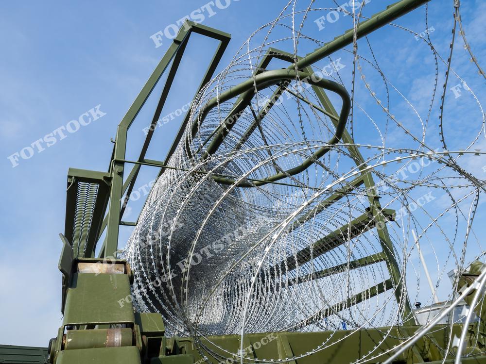 На изображении крупным планом показана катушка колючей проволоки, установленная на военной технике. Фотография символизирует использование защитных барьеров для укрепления позиций и ограничения доступа. Проволока свернута в компактную конструкцию, готовую к развертыванию.