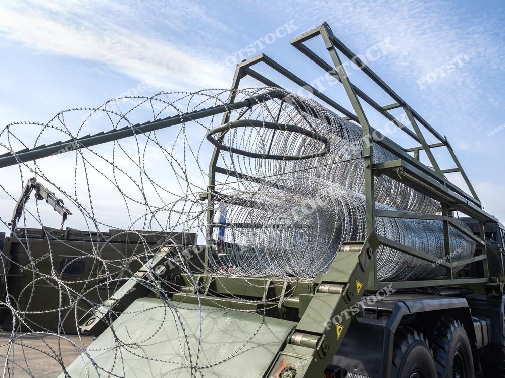 На фотографии изображена катушка колючей проволоки, установленная на военной машине. Конструкция предназначена для быстрого развертывания защитных барьеров в полевых условиях. Фотография подчеркивает тактические и инженерные решения для обороны.