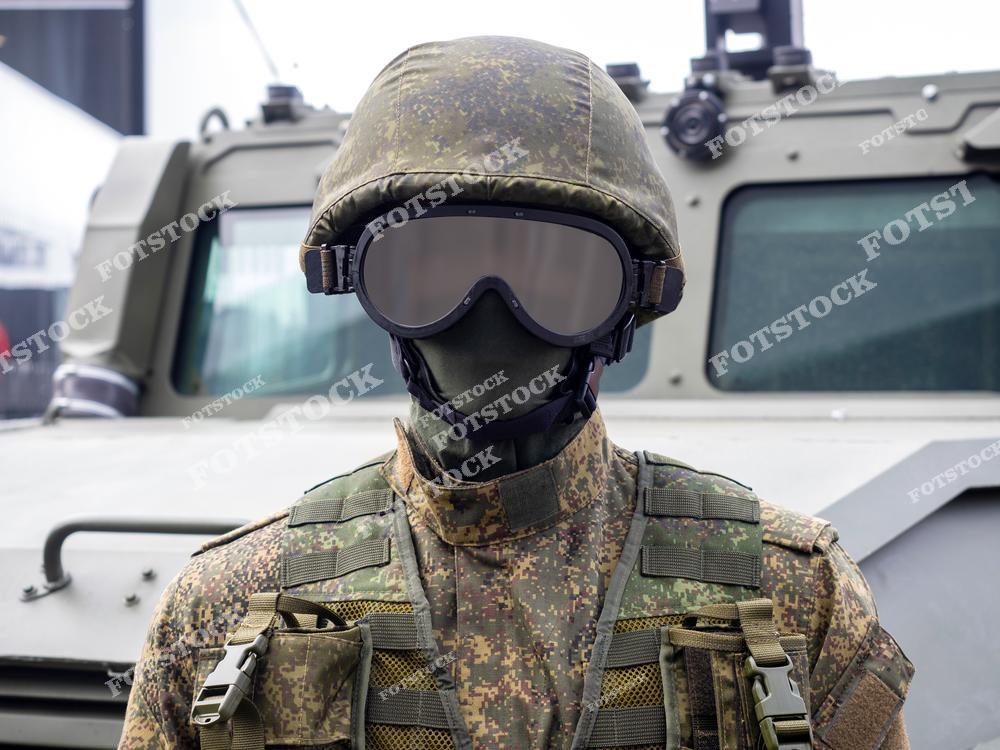 На фотографии изображен военнослужащий в камуфляжной форме, защитном шлеме и очках, стоящий перед бронемашиной. Экипировка подчеркивает современное оснащение и тактическую готовность. Снимок символизирует оборонительные технологии и защитные меры.