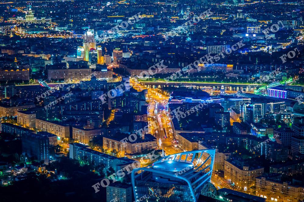 На фотографии представлен ночной панорамный вид Москвы, снятый с высоты. В центре композиции выделяется сталинская высотка — здание Министерства иностранных дел. Чётко прослеживаются ярко освещённые городские магистрали, уходящие вдаль. Архитектура Москвы представлена как современными, так и историческими строениями. Всё пространство города охвачено мягким светом улиц, рекламы и подсветки зданий.