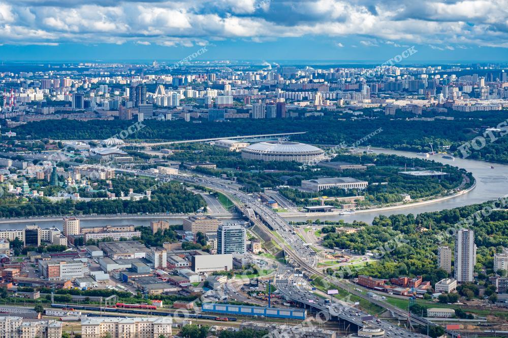 На фотографии представлен панорамный вид Москвы, снятый с высоты. Яркий солнечный день с голубым небом и белыми облаками делает пейзаж насыщенным и живописным.