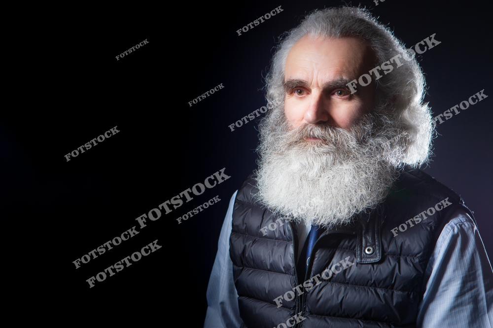 Фотоснимок показывает пожилого мужчину около 70 лет с большой седой бородой, где изображение подчёркивает его возраст, жизненный опыт и выразительный внешний вид. Эта фотография выглядит как характерная портретная иллюстрация, а картинка создаёт спокойный и уважительный слайд образа дедушки.