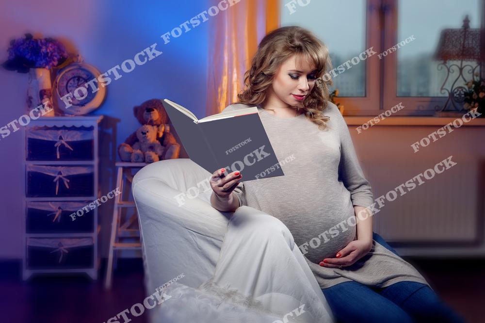 На изображении — беременная женщина, сидящая в кресле и читающая книгу, одной рукой она держит живот. Интерьер оформлен мягкими тонами, с игрушками и элементами уюта, создавая атмосферу тепла и спокойствия. Сцена символизирует гармоничное ожидание ребёнка, любовь и внутреннюю подготовку к материнству.